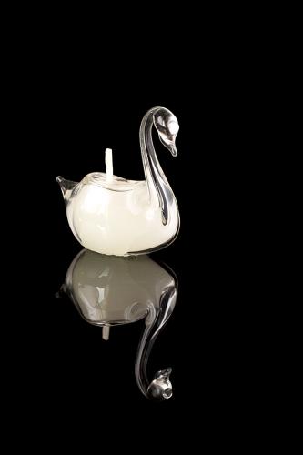 A glass swan figure candle on a black mirror surface