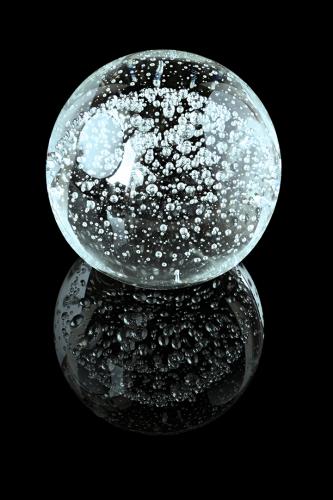 A glass ball with inner bubbles on a black mirror surface