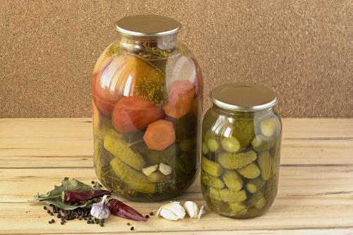 A glass jars with salted cucumbers and tomatoes and some spices