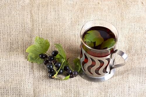 Black tea with black currant leaves in a glass and some black cu