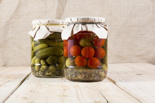 Canned cucumbers and tomatoes in two glass banks on a wooden boa