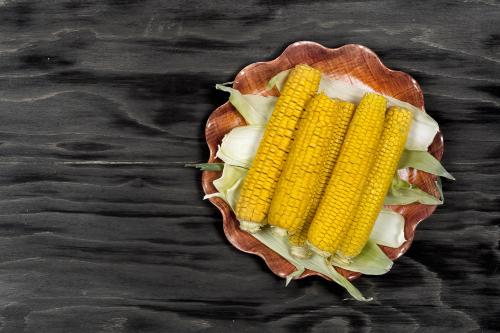 Fresh boiled corn on the cobs on a black wooden surface