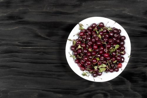 Ripe red cherry in white dish on a black wooden surface