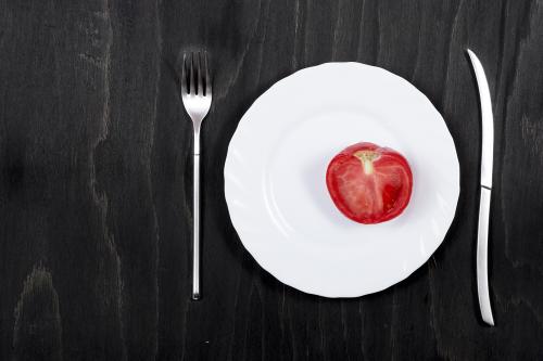 Half of red tomato on a white plate on a black wooden surface