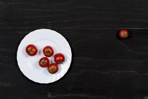 Red tomatoes and white dish on a black wooden surface