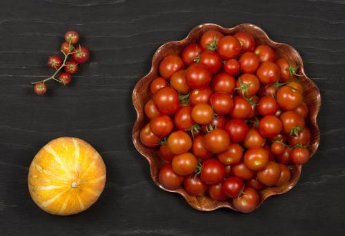 Ripe orange pumpkin and red tomatoes on a black wooden surface