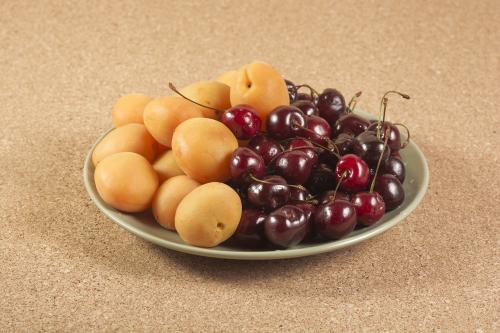 Ripe apricots and cherry on a green ceramic plate on a cork surf