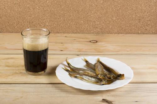 Some smoked capelins on a white plate and a glass of dark beer o