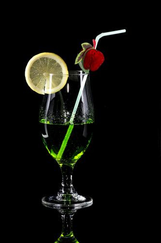 Glass of green drink with bendie on black mirror background
