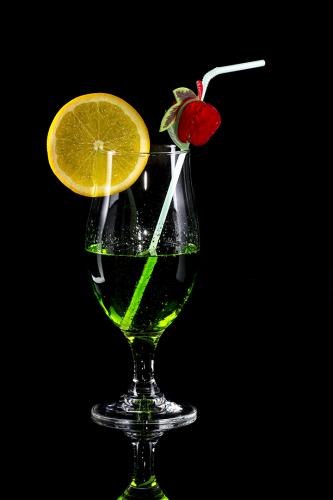 Glass of green drink with bendie on black mirror background